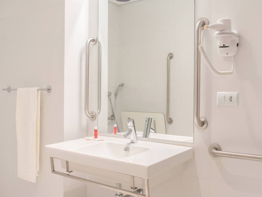 A bathroom with a white sink, a mirror, a handheld showerhead, and a wall-mounted hairdryer.