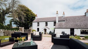 An outdoor patio area with wicker furniture and a glass table, in front of a white building with a grey roof. - The Manor House - UK6741 (Lydstep, near Tenby)