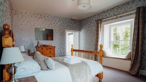 A bedroom with a bed, wooden headboard, dresser, lamp, and a window with curtains. - The Manor House - UK6741 (Lydstep, near Tenby)