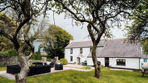 A white building with a grey roof, surrounded by a grassy lawn and trees. - The Manor House - UK6741 (Lydstep, near Tenby)