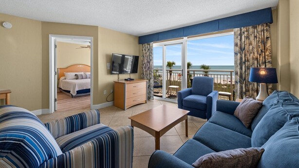 Quarto de hotel com varanda, uma cama, televisão, sofá e mesa de centro.