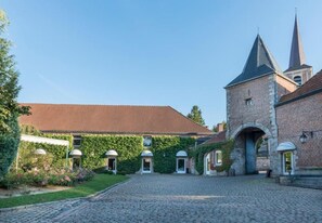 A courtyard with a cobblestone path leading to a brick building with a tower and a church spire. - Logis Hotel La Gentilhommiere (Nouzerines)