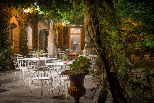 An outdoor dining area with tables and chairs, surrounded by greenery and stone walls. - Logis Hotel La Gentilhommiere (Nouzerines)