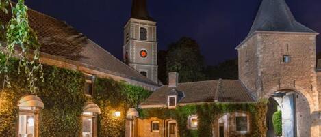 Un edificio histórico con una torre de reloj, muros cubiertos de hiedra y un patio empedrado.