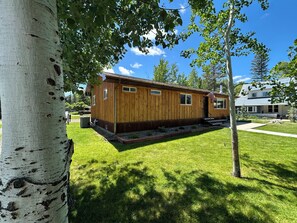 A wooden cabin with a small porch, a flag, and a well-maintained lawn.