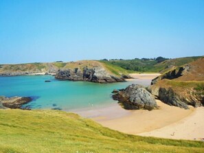 Un paysage côtier avec une plage de sable, des affleurements rocheux et une mer bleue et limpide.