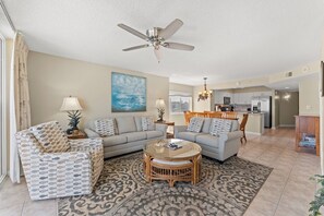 A living room with a sofa, armchairs, a coffee table, a ceiling fan, and a painting.