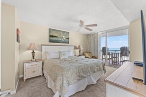 A bedroom with a bed, nightstands, a ceiling fan, a painting, and a balcony with chairs.