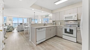 A modern kitchen with a central island, built-in appliances, and a view to the outside. - 4-bedroom, 3-bathroom, family-friendly oceanfront condo, 9th floor views | Windy Hill Dunes - 906 (North Myrtle Beach)