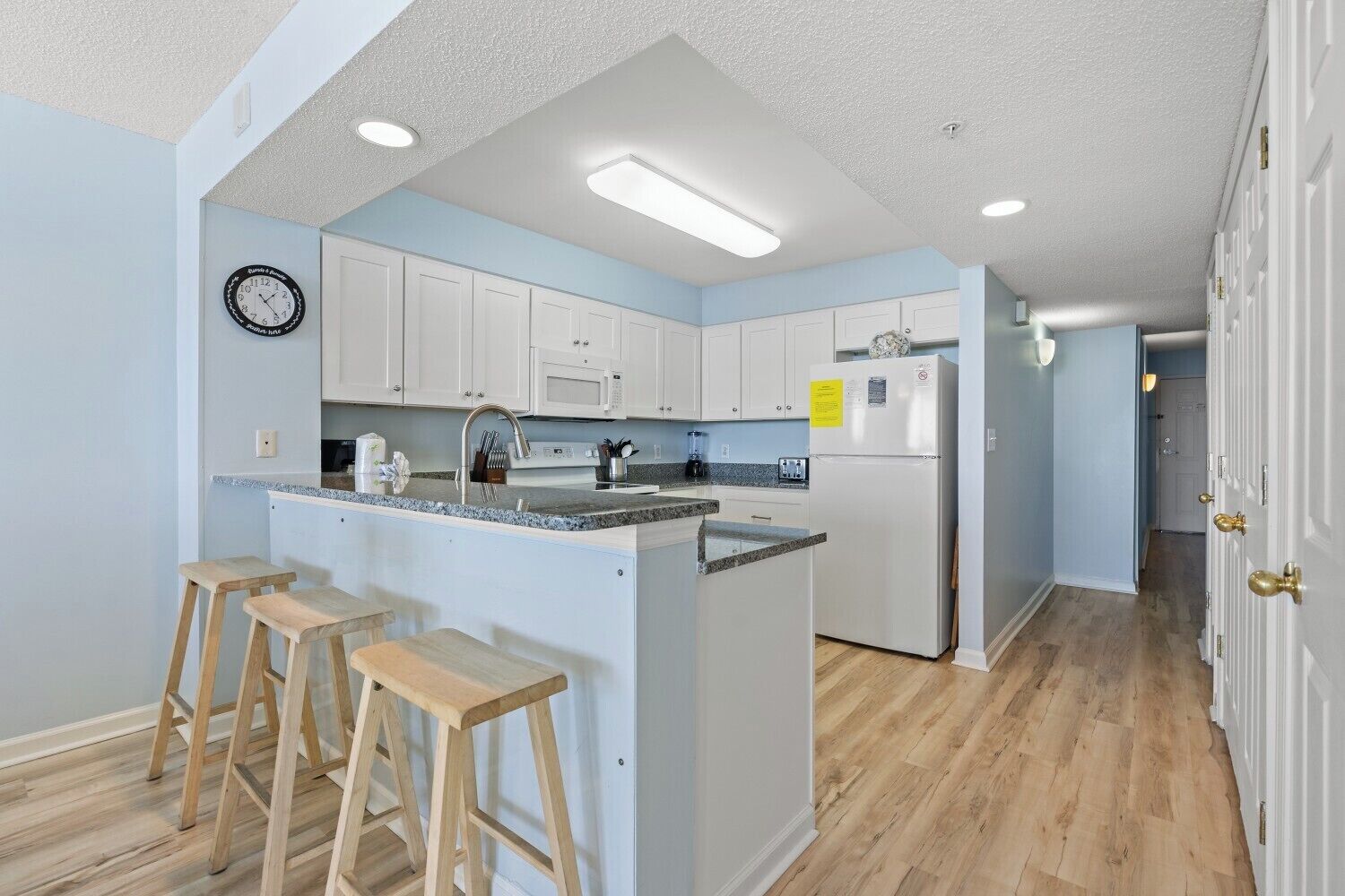 A modern kitchen with white cabinets, a granite countertop, and a built-in island with bar stools.