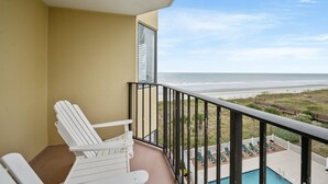 Ein Balkon mit weißen Stühlen, einem Pool und Blick auf Strand und Meer.