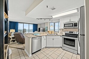 A modern kitchen with stainless steel appliances, a large island, and a view to the outside. - Beautiful 4th Floor Condo, Outdoor Pool and Hot Tub | Spinnaker - 405 (North Myrtle Beach)