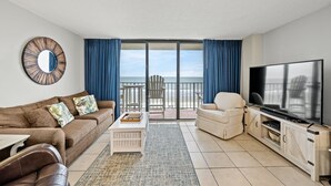 Ein Wohnzimmer mit Sofa, Sessel, Couchtisch, Fernseher und Meerblick durch große Schiebetüren.