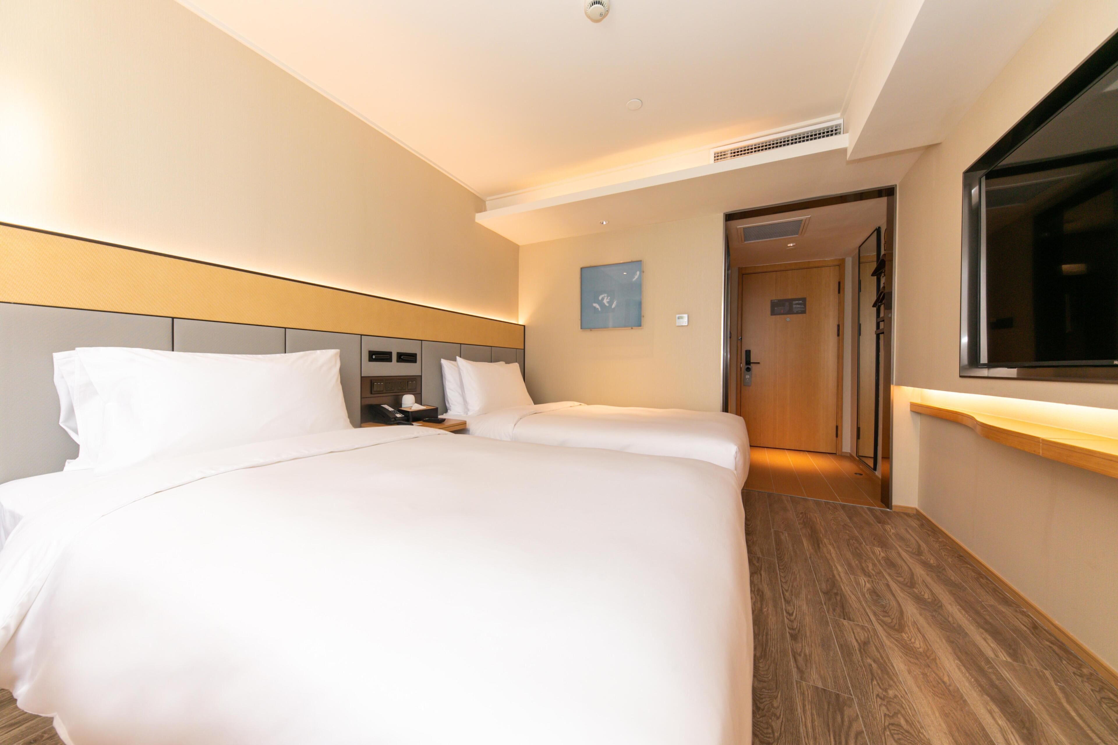 Una habitación de hotel con una cama grande, una mesita de noche, un televisor y piso de madera.