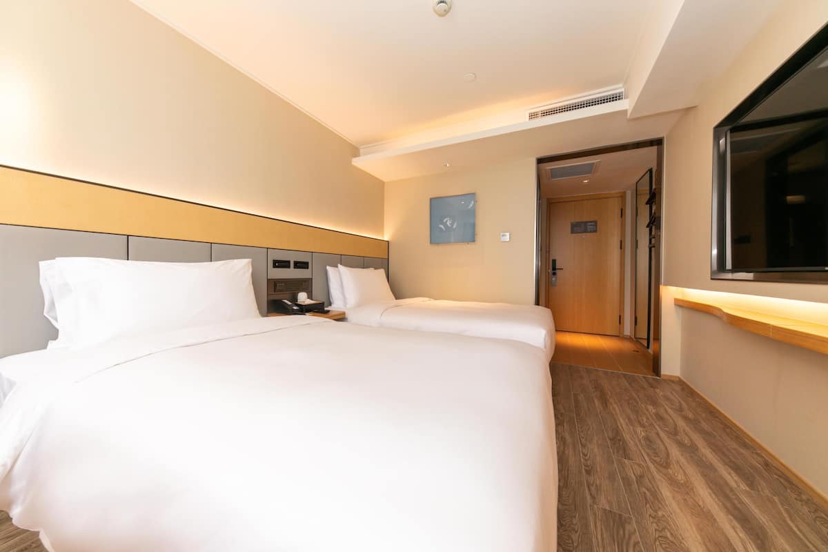 A hotel room with a large bed, a bedside table, a TV, and a wooden floor.