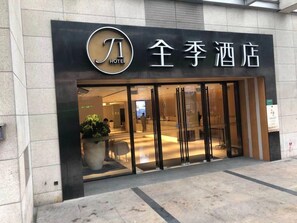 Entrada de hotel con diseño moderno, destacando un logotipo e indicaciones en inglés y chino.