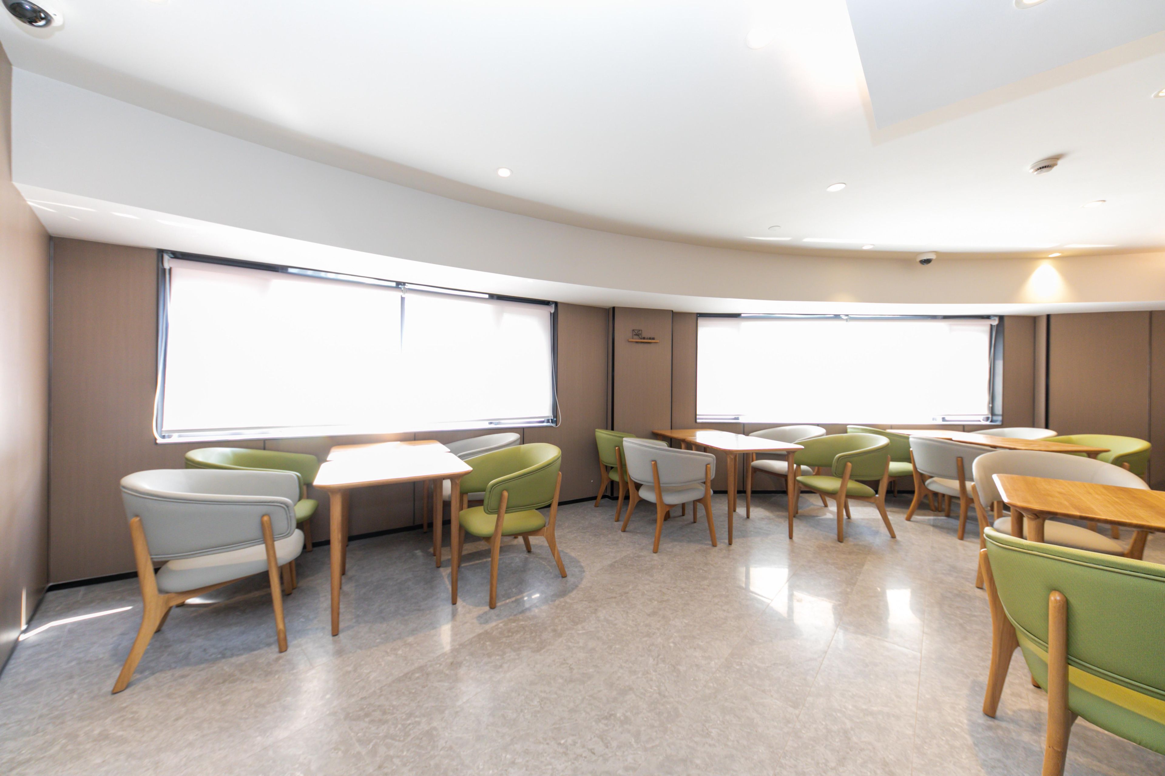 A modern interior with a curved layout, large windows, and a mix of green and white chairs around tables.
