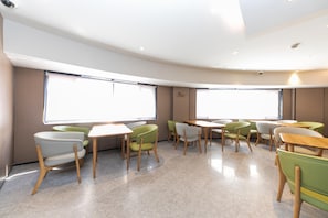 A modern interior with a curved layout, large windows, and a mix of green and white chairs around tables.