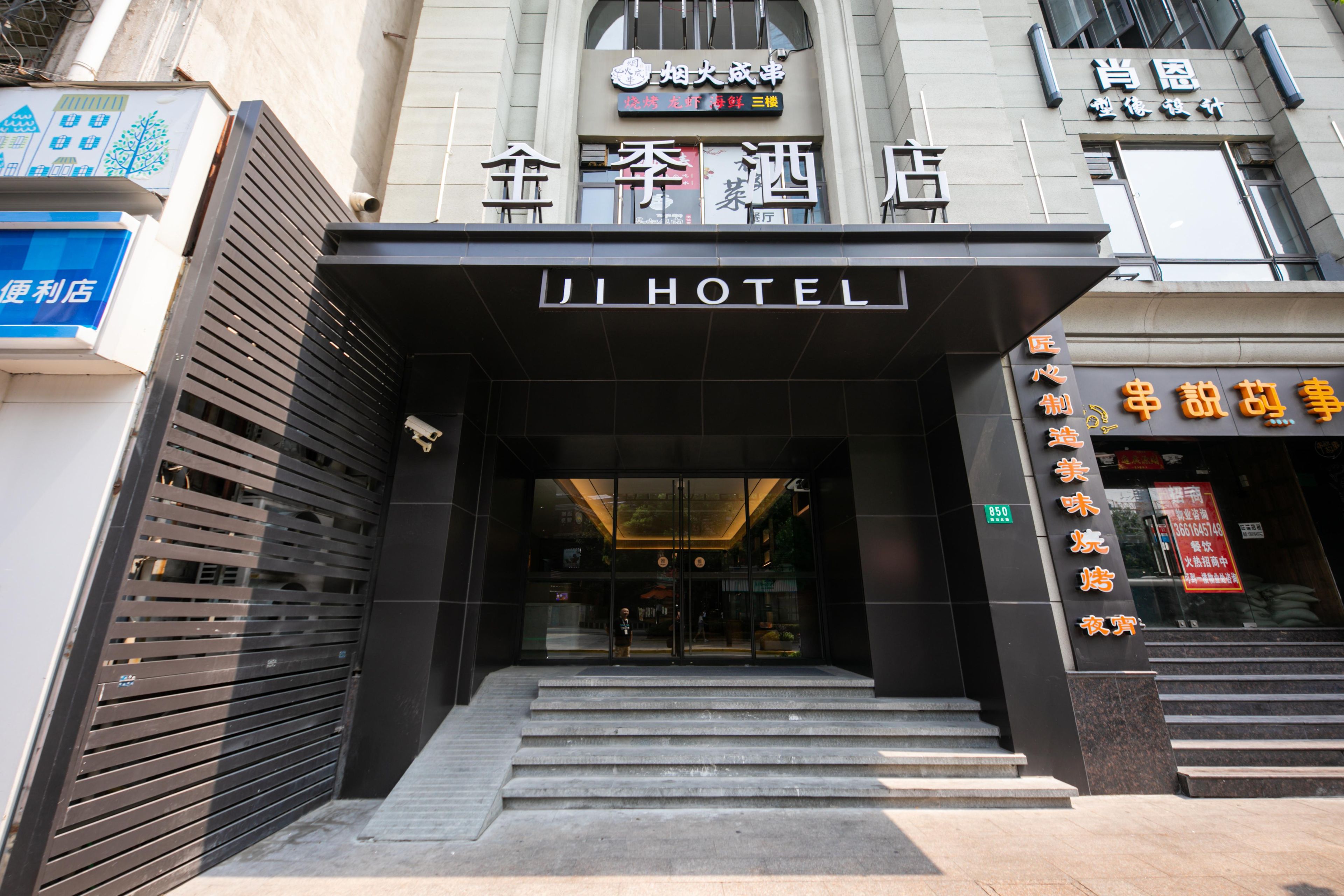 Entrada de un hotel con fachada negra, puertas de vidrio y una escalera que sube.