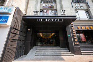 A hotel entrance with a black facade, glass doors, and a staircase leading up.