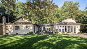 A two-story house with a well-maintained lawn and a large tree in front.
