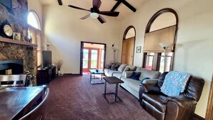 A spacious living room with a stone wall, a ceiling fan, a fireplace, a sofa, a leather armchair, and a television.