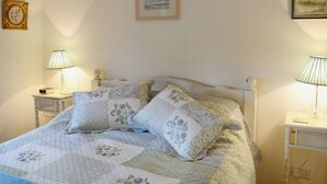 Una cama bien hecha con ropa de cama floral, dos lámparas de noche, un cuadro en la pared y una mesita con un reloj y una lámpara.