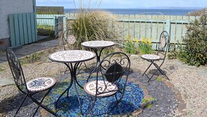 Un patio con cuatro mesas redondas y sillas, una cerca de madera y vistas al mar.