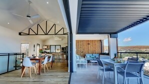 A modern dining area with a wooden table and chairs, a kitchen in the background, and a balcony with a view of the landscape. - La Villa Azur Saint-Gilles ***** - Reunion Island - Seaview, Pool, Beach & BBQ! (Saint-Gilles les Bains)