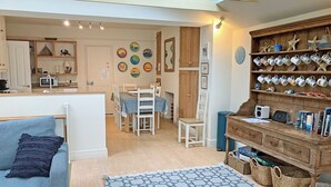 A cozy living room with a blue sofa, a dining area with a table and chairs, a kitchen with a microwave, and a bookshelf filled with decorative items. - 4 bedroom accommodation in Church/Market (Church/Market)