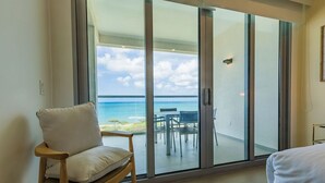 A room with a large sliding glass door leading to a balcony with a view of the ocean.