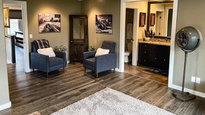 Uma sala de estar moderna com duas poltronas, um chão de madeira escura e um espelho grande sobre a pia.