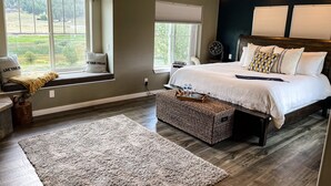 Quarto com cama grande, um assento junto à janela com vista, ventilador de teto e piso de madeira.
