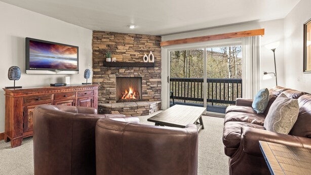Una sala de estar con chimenea de piedra, mobiliario de cuero, televisor de pantalla plana y un balcón con barandilla.