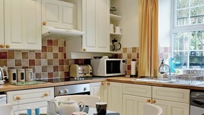 Een keuken met witte kastjes, een magnetron, een waterkoker en een spoelbak.