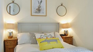 Een netjes opgemaakt bed met een witte dekbedovertrek en een geel kussen, met aan weerszijden twee nachtkastjes met lampen, en twee spiegels aan de muur.