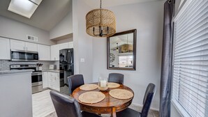 Une cuisine moderne avec des meubles blancs, des appareils en acier inoxydable et un coin repas comprenant une table et des chaises en bois.