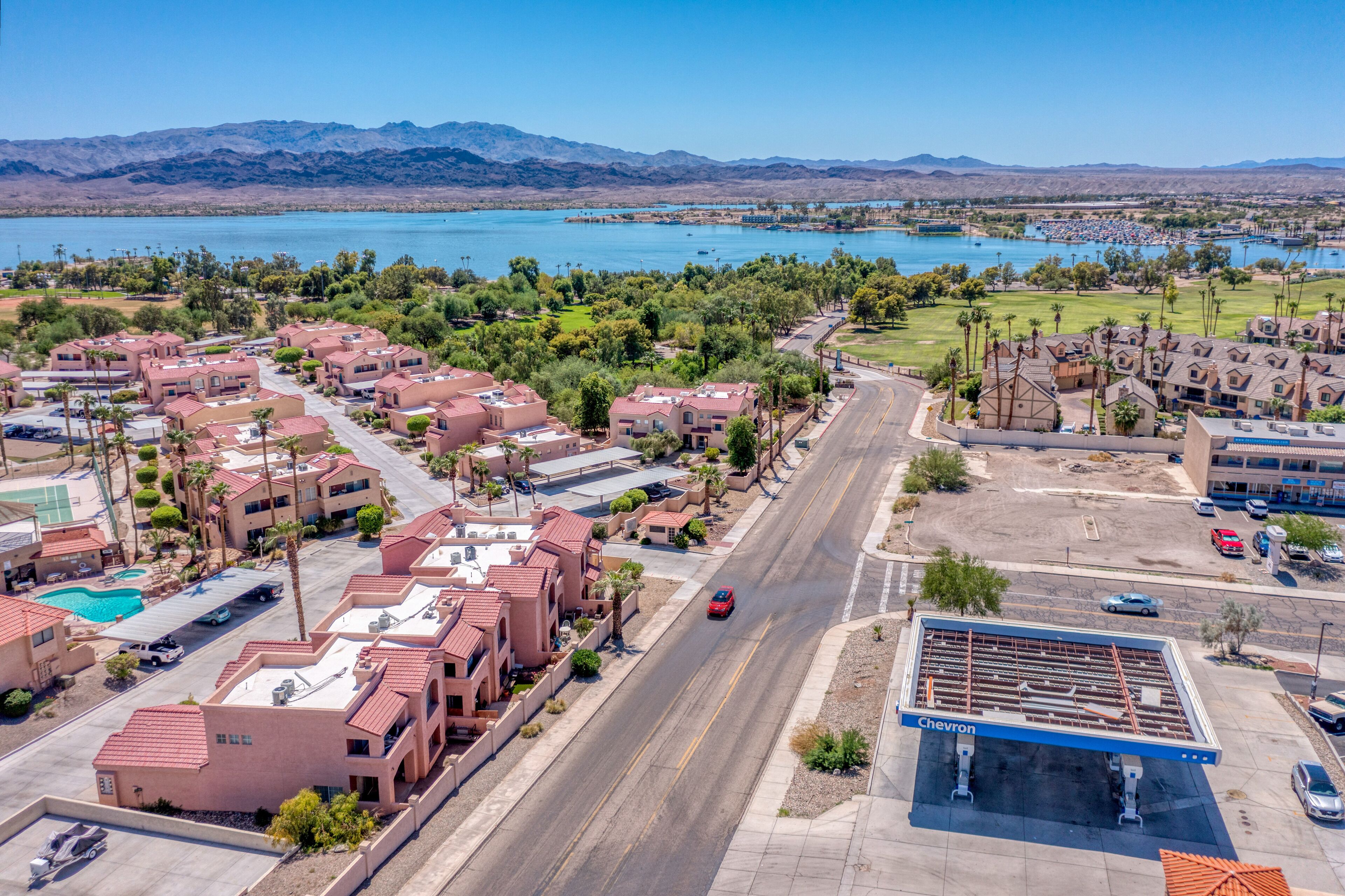 Zona residencial com posto de gasolina Chevron, piscina e vista para um lago com montanhas ao fundo.
