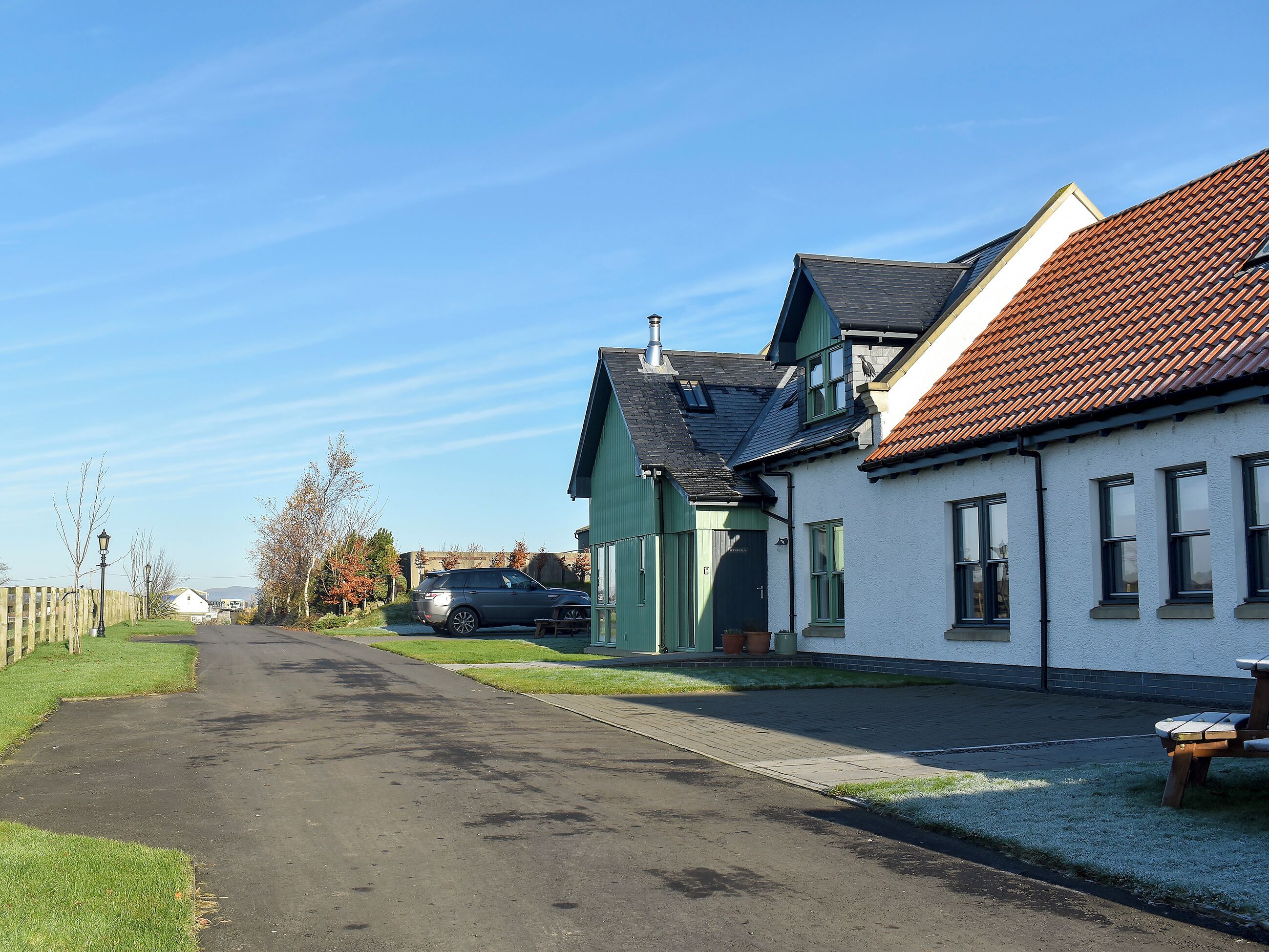 A quiet street with houses, a parked car, and a bench.