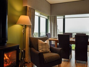 Ein gemütlicher Raum mit Kamin, Tisch mit Stühlen und Blick durch große Fenster.