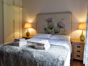Ein Schlafzimmer mit einem Bett, zwei Nachttischen mit Lampen, einem Kopfteil mit floralem Dekor und einem Kleiderschrank.