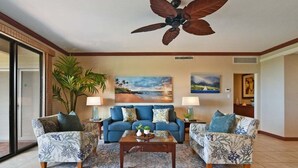Un salon avec un canapé bleu, deux fauteuils, une table basse et un ventilateur de plafond.