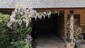 A rustic wooden building with a gravel driveway and a hanging flower arrangement.