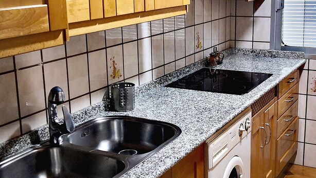 A compact kitchen with wooden cabinets, a double sink, a built-in oven, and a washing machine.