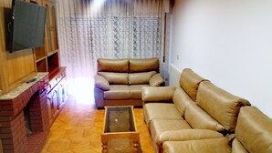 A living room with a leather sofa, a small wooden coffee table, and a television mounted on the wall.