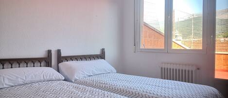 A bedroom with two beds, a window, and a radiator.
