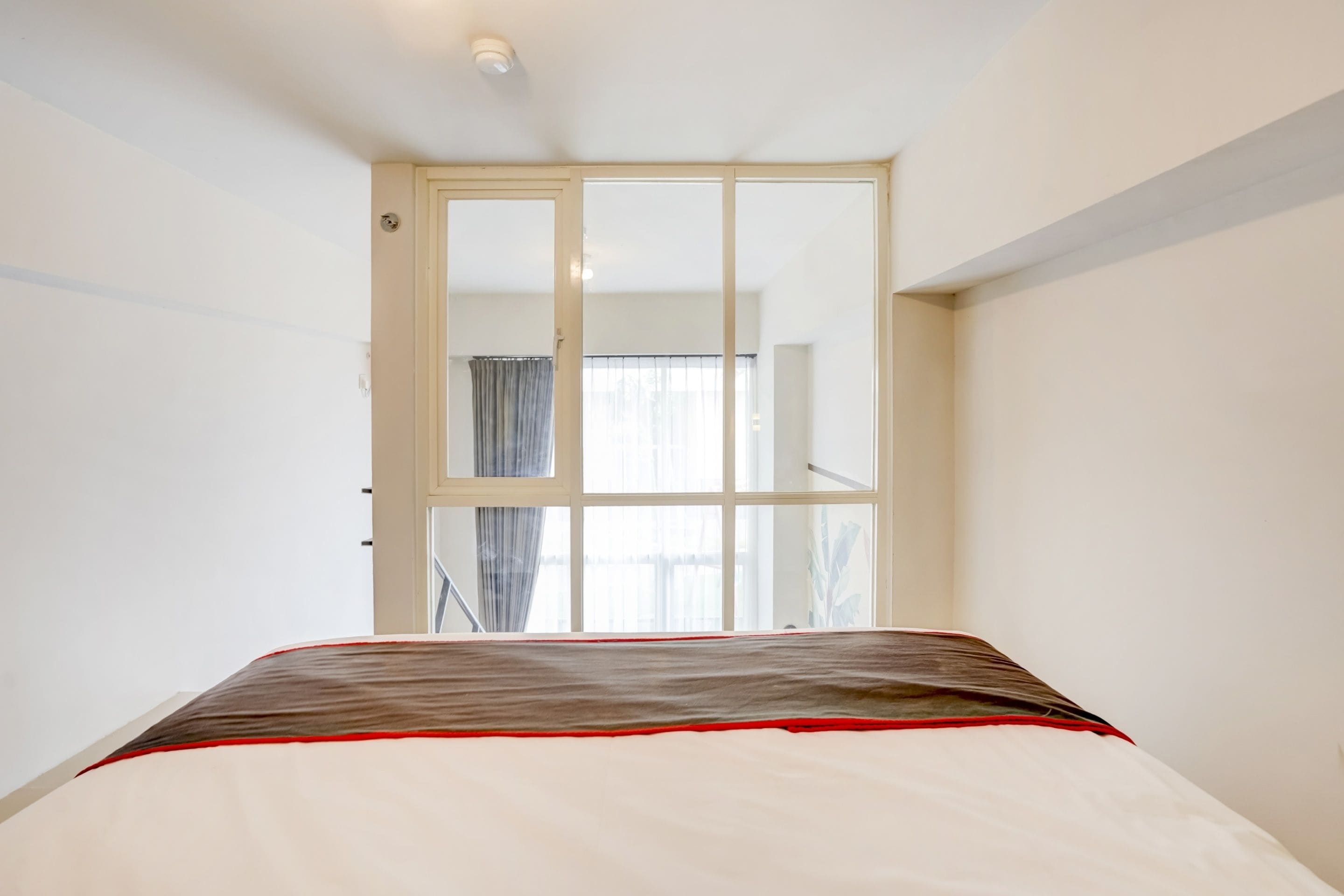 A bedroom with a bed, a window, and a door leading to another room.