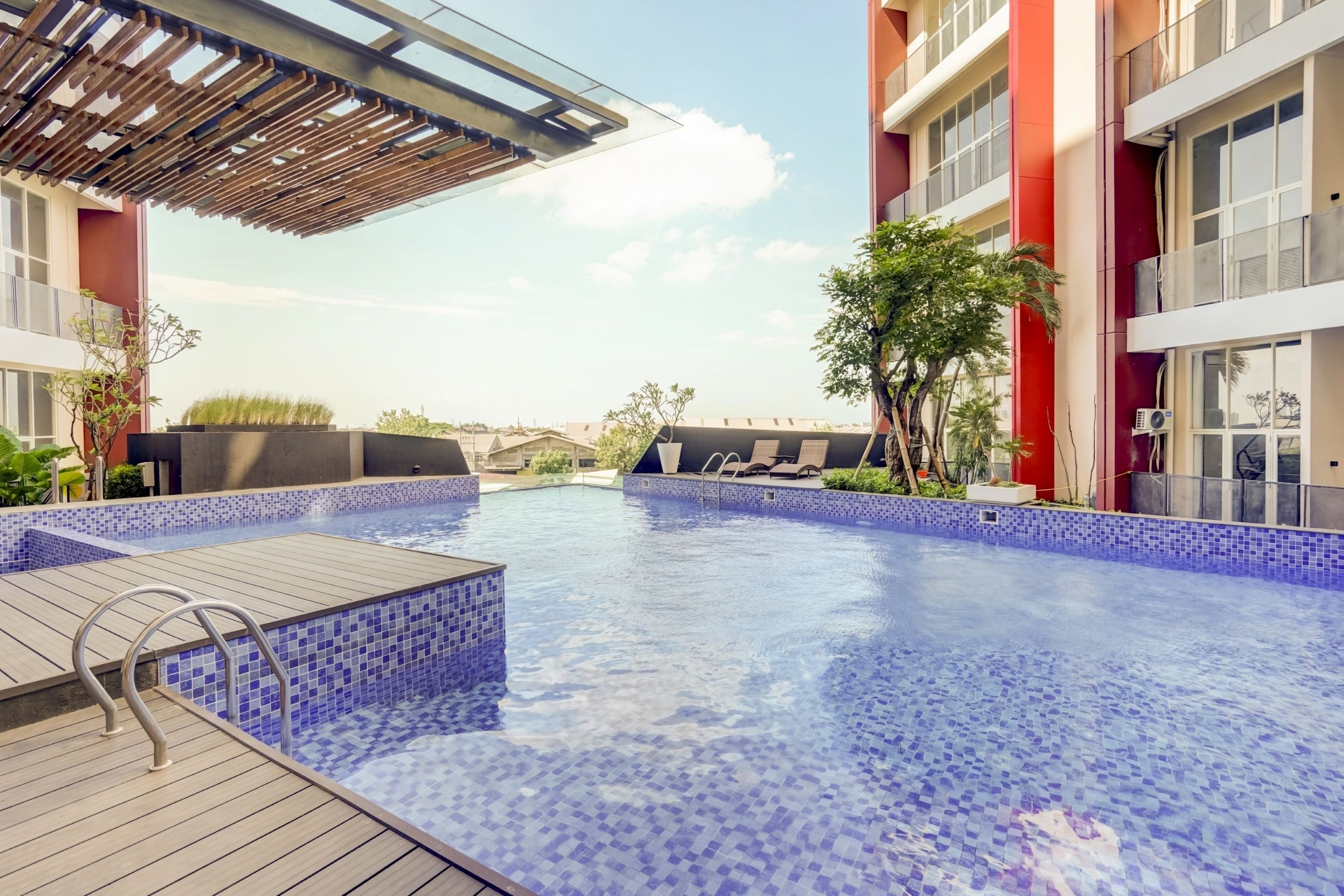 A swimming pool with tiled edges, wooden deck, and metal railings.