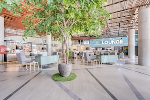 A spacious lounge area with seating arrangements, a reception desk, and a large potted tree. - Super OYO Collection O 30 Amega Crown Sub (Surabaya)