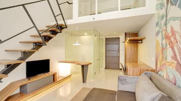 A modern living space with a staircase, a flat-screen TV, a sofa, and a glass door leading to another room.